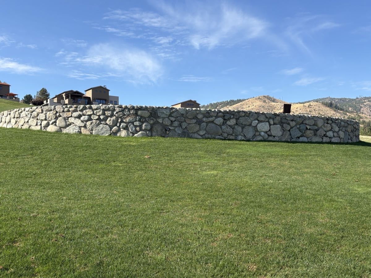 Long granite boulder retaining wall above a level lawn