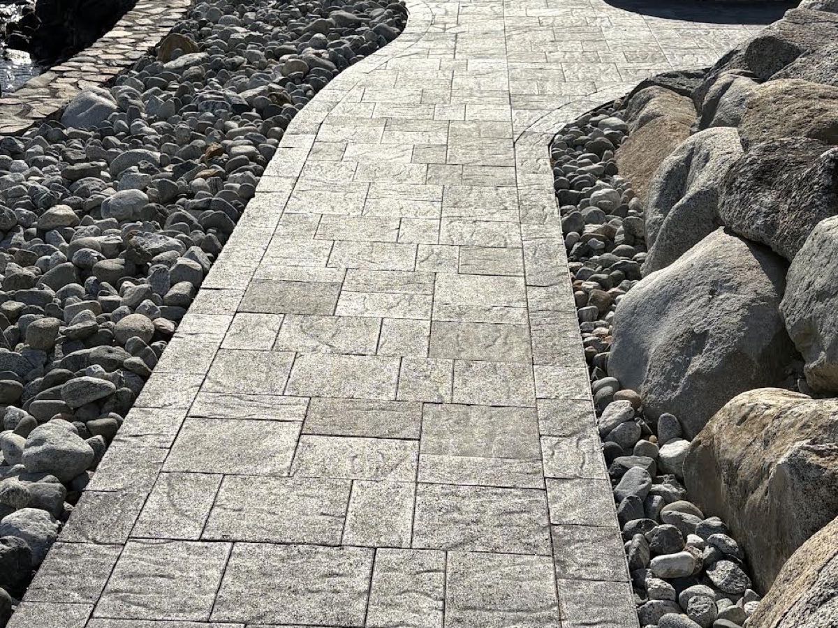 Stamped concrete walkway winding between river-rock beds and boulders